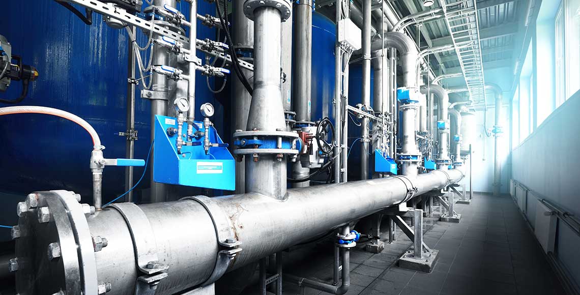 Large industrial water treatment and boiler room. Shiny steel metal pipes and blue pupms and valves.